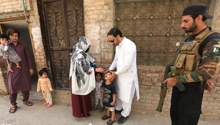 Security personal stand alert while health worker administrating polio drops to a child during anti-polio campaign at Dalaz road on April 22, 2025. — INP