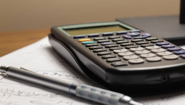 This representational image shows a calculator lays on the table next to the pen. — Unsplash/File