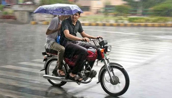 A motorcyclist and a pillion rider protect themselves with an umbrella during heavy rain in Lahore on May 2, 2023. — Online