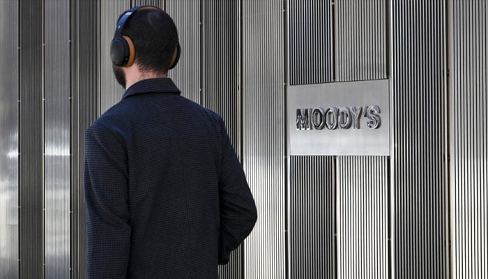 A person wearing headphones crossing by Moodys logo. —AFP/File