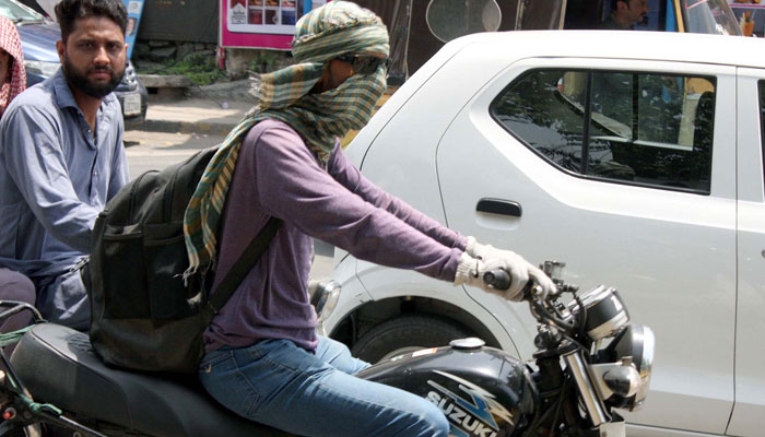 Commuter cover face and head with the wet cloth passing through the road trying to escape from scorching sun during a hot day of summer season, in Lahore on May 21, 2025. — PPI