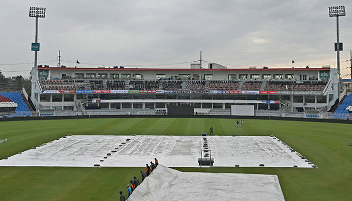 Ground staff members cover the field with a plastic sheet following rain showers at a cricket stadium. — AFP/File