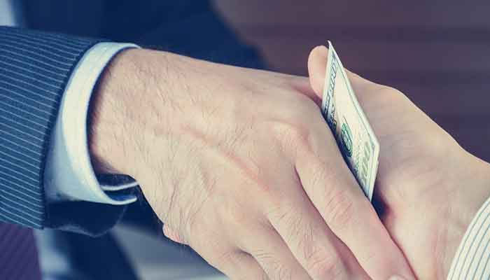 A representational image of two persons shaking hands keeping dollar bill in between. —TheNews/File
