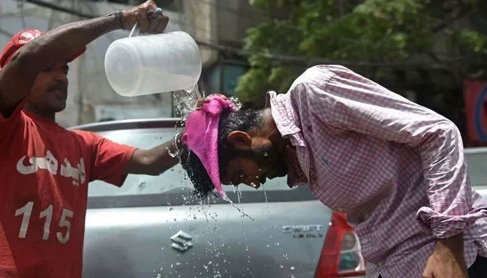 An Edhi volunteer pours water on a pedestrian along a street during a hot summer day. — AFP/File