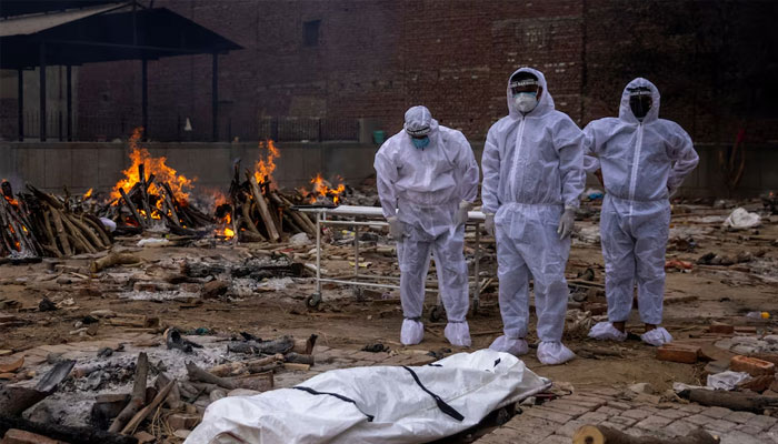 Men wearing protective suits stand next to the body of their relative, who died from the coronavirus disease (COVID-19), before her cremation at a crematorium ground in New Delhi, India, May 4, 2021.—Reuters
