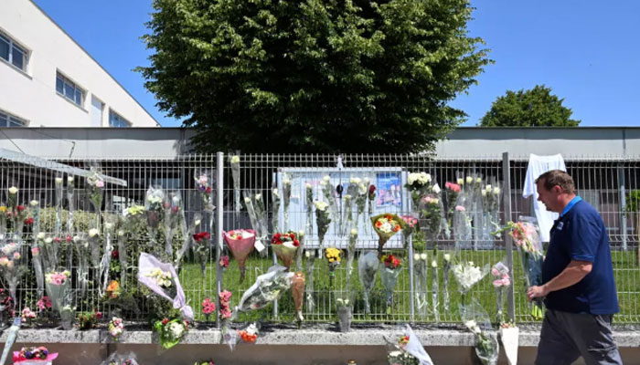 A man walks past flowers on the fence of Francoise Dolto middle school in Nogent on June 11, 2025.— AFP