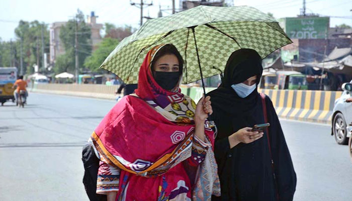 Students are walking under an umbrella to protect themselves from direct sunlight during hot weather. — APP/File