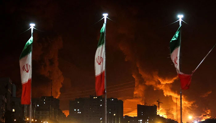 Iranian flags fly as fire and smoke from an Israeli attack on Sharan Oil depot rise, following Israeli strikes on Iran, in Tehran, Iran on June 15, 2025. — Reuters