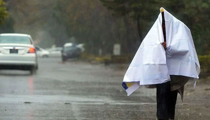 A man covers himself with a sheet while walking on the road during a rainy day. — AFP/File