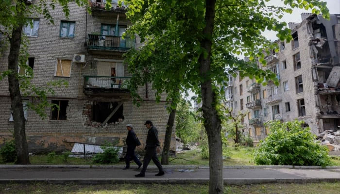 Men walk past a damaged residential building in the town of Lyman, near the frontline in the Donetsk region, on May 7, 2025 amid the Russian invasion of Ukraine. — AFP