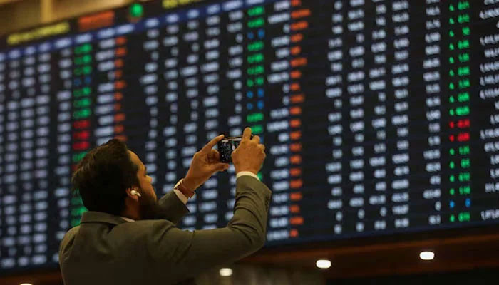 A man takes a photo of the electronic board at the Pakistan Stock Exchange in Karachi on November 28, 2023. — Reuters