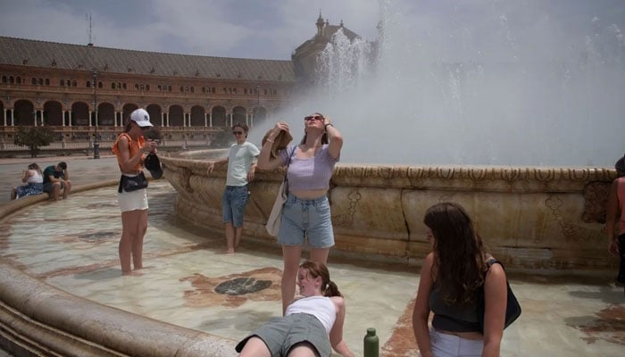 In this picture people cool off with a water fountain during a heat wave in Seville, Spain. &mdash; AFP/File