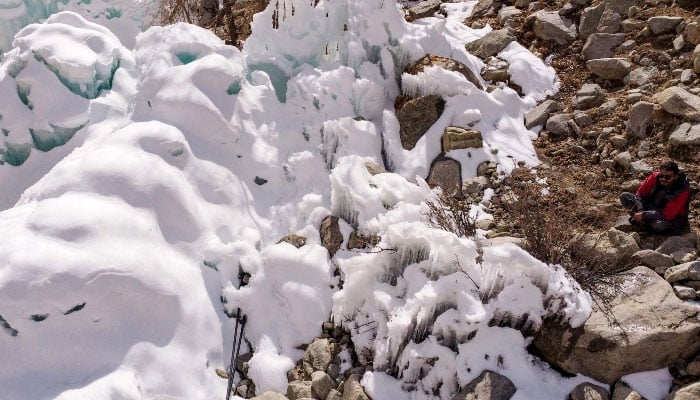 This aerial photograph, taken on March 18, 2025, shows a man (right) looking at an artificial glacier built by local residents during winters to conserve water for the summers at Pari village in Kharmang district, in the mountainous Gilgit Baltistan region. &mdash; AFP