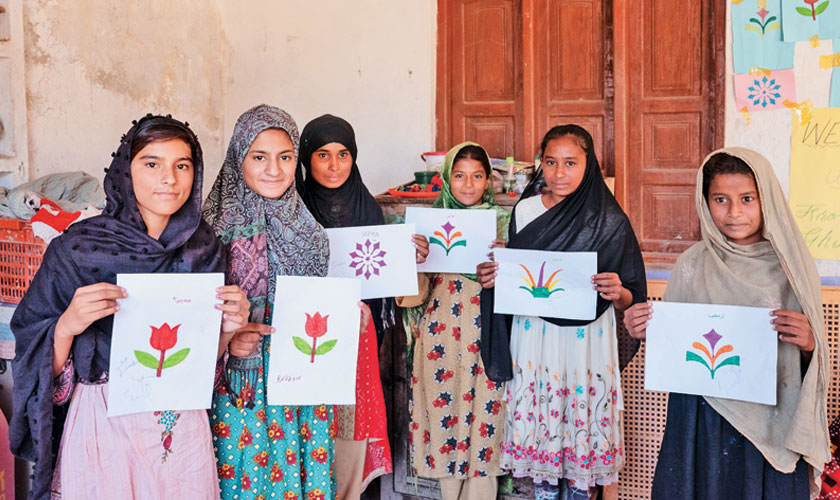 Madiha 14 (black dupatta), Rukhsar 14 (green), Waseema 14 (White) and a few other girls hold up the drawings they just made during a visit from the Mobile and Static Child Safe Space.