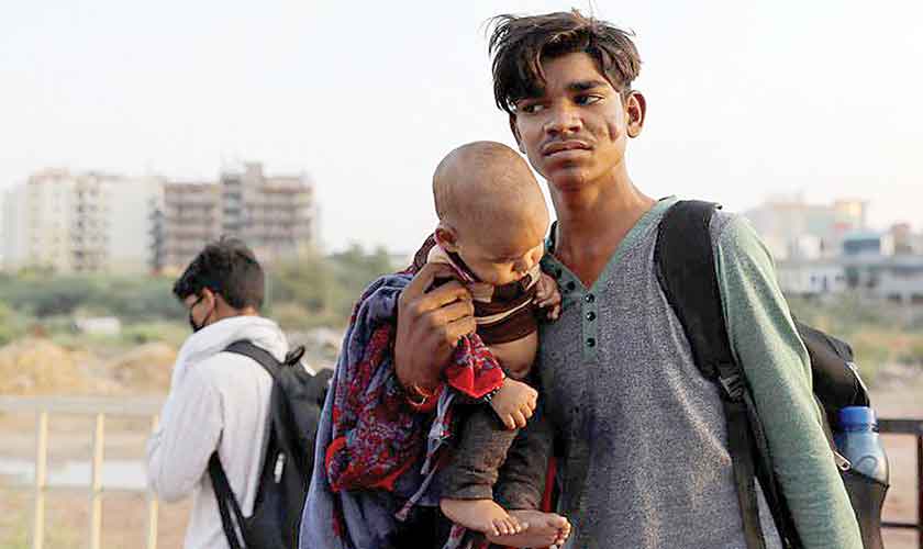 An migrant worker carries his child, as they wait to cross the border to their home state of Uttar Pradesh, in New Delhi.