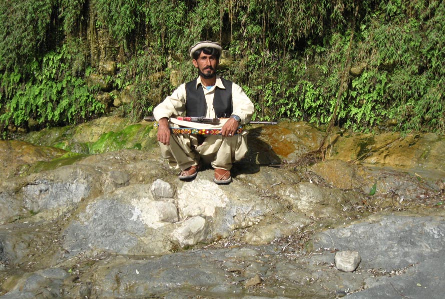 Izzat Gul posing for a photo in front of the green wall.