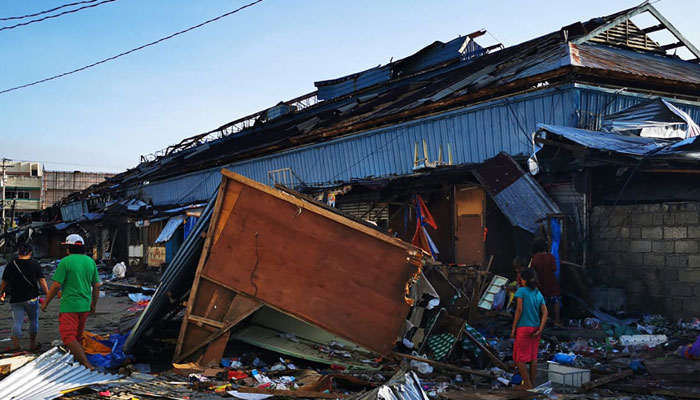 Residents walk past debris next to a damaged building in Surigao City, Surigao del Norte province on December 18, 2021, days after Super Typhoon Rai passed over the city. — AFP/File
