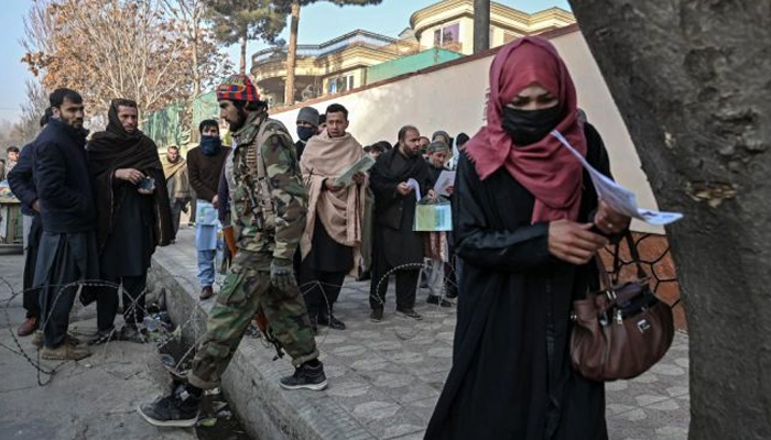A Taliban member walks past people waiting to enter the passport office at a checkpoint in Kabul on December 19, 2021, after Afghanistan’s Taliban authorities said they will resume issuing passports. — Photo by Mohd Rasfan/AFP via Getty Images