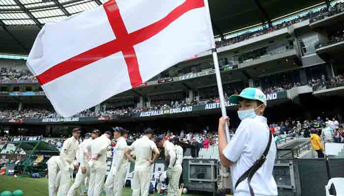 A masked flag bearer holds the flag as the England team prepare to enter the field for the second session during the second day of the third Ashes cricket Test match between Australia and England in Melbourne on December 27, 2021. -AFP
