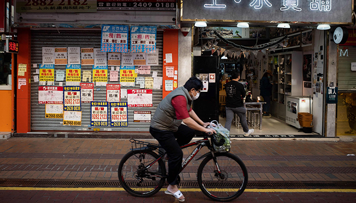 This photo taken on December 10, 2021 shows a man riding a bicycle past the BeWater Mart retail store (R) operating next to an empty shoplot in Sheung Shui, a town in northwest Hong Kong near the border with mainland China. — AFP/File