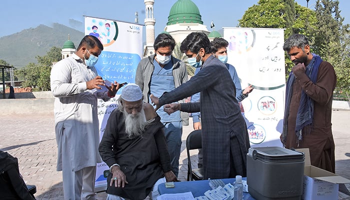 Workers of a mobile vaccination team administering coronavirus vaccine to an elderly man at the Shrine of Bari Imam in Islamabad, on November 31, 2021. — Online/File
