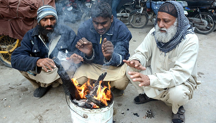 People sitting around a fire to keep them warm during chilly weather in Karachi. — APP/M Saeed Qureshi