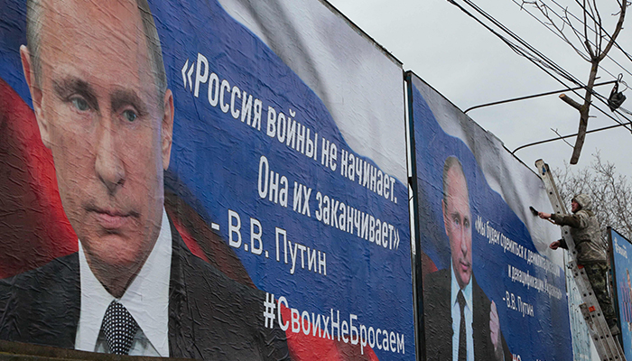 A man finishes glueing huge placards bearing images of Russian President Vladimir Putin and reading Russia does not start wars, it ends them (L) and We will aim for the demilitarisation and denasification of Ukraine in the city center of Simferopol, Crimea, on March 4, 2022. — AFP