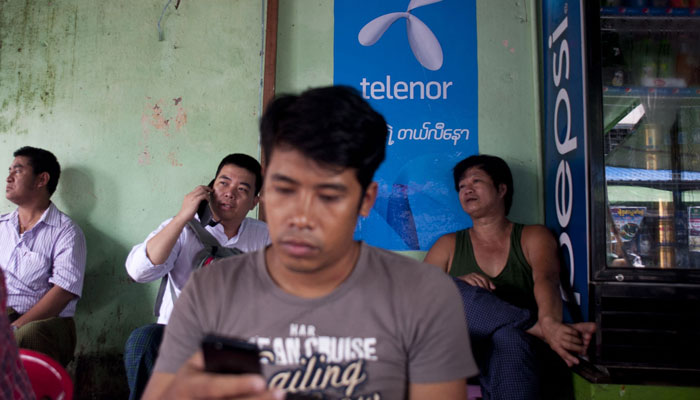 In this file photo taken on September 26, 2014, a man uses a mobile phone in front of a Telenor advertising board in Yangon. Myanmars junta has approved the sale of Norwegian telecoms giant Telenors Myanmar subsidiary to Lebanons M1 group, both companies said on March 18, 2022. Photo: AFP