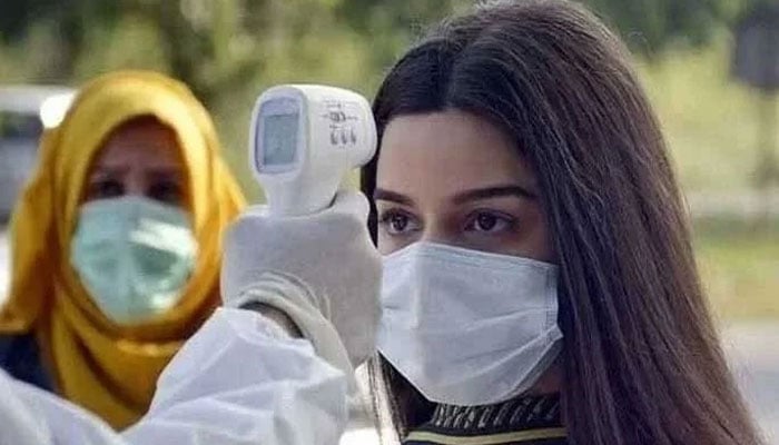 A paramedic checks body temperature of a woman with a temperature gun. Photo: Geo.tv/ file