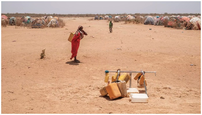 A woman carries a container of water on her back in a desert. — AFP