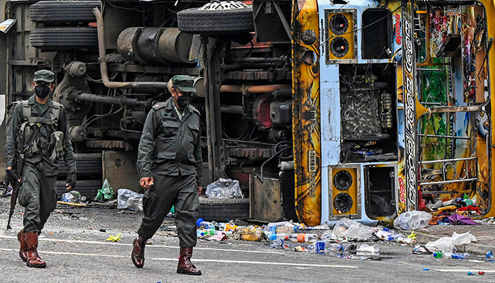 Security personnel walk past a burned vehicle along a road, a day after they were torched by protesters in Colombo on May 10, 2022. — AFP