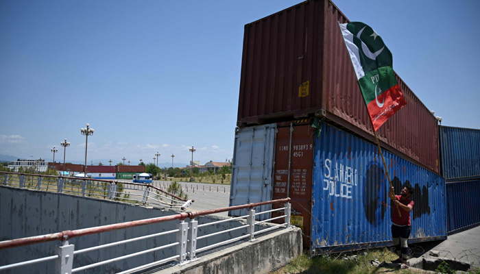 A supporter of PTI party, waves flags beside containers stacked by the authorities to block the Red Zone ahead of the sit-in planned in Islamabad on May 24, 2022. -AFP