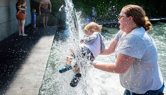 A woman holds a young child under a waterfall at a park in Washington, DC, on June 28, 2021, as a heatwave moves over much of the United States. — AFP