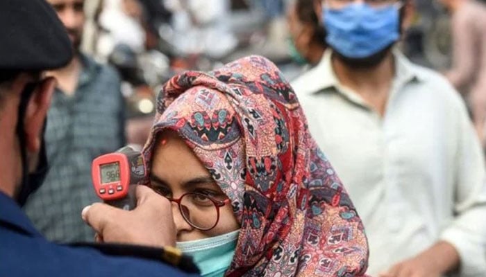 A shopping mall official (L) checks the body temperature of a customer in Karachi. — AFP/File