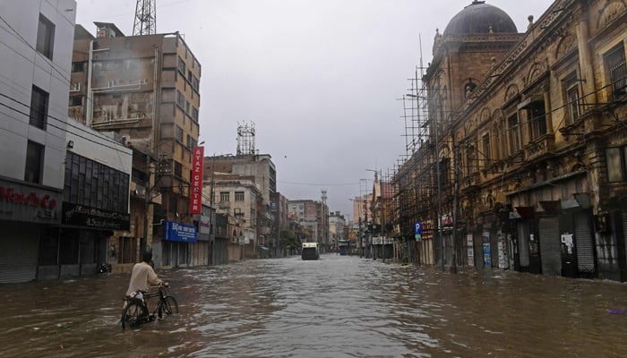 A commuter makes his way through a flooded street after a heavy rain shower in Karachi on July 11, 2022. -AFP