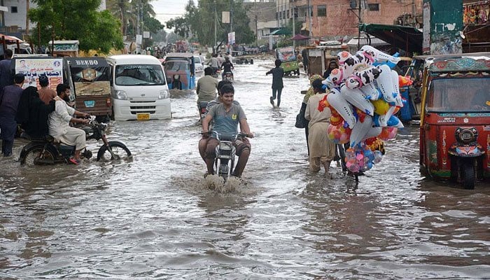 Motorcyclists passing through rainwater accumulated on a road in Korangi area of Karachi on July 9, 2022. Photo: APP