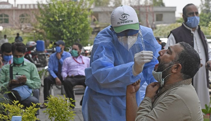 A health official wearing protective gear takes the sample of a man at a drive-through screening and testing facility for COVID-19, alongside a street in Islamabad. Photo: AFP/file
