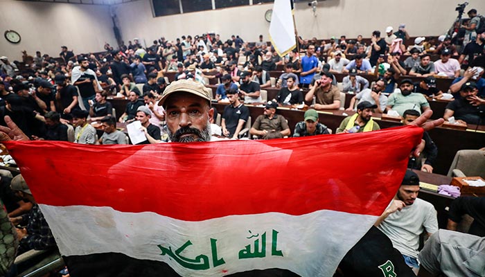 A man deploys a national flag as supporters of the Iraqi cleric Moqtada Sadr gather inside the country´s parliament in the capital Baghdad´s high-security Green Zone, to protest against a rival bloc´s nomination for prime minister, on July 30, 2022. — AFP