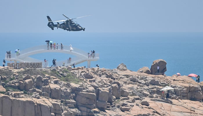 Tourists look on as a Chinese military helicopter flies past Pingtan island, one of mainland China´s closest point from Taiwan, in Fujian province on August 4, 2022, ahead of massive military drills off Taiwan following US House Speaker Nancy Pelosi´s visit to the self-ruled island.-AFP