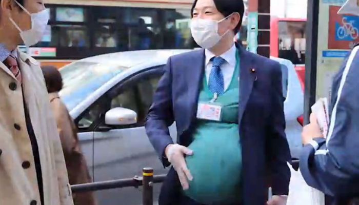 Masanobu Ogura who is minister in charge of dealing with Japans failing birthrate tryinh out a pregnancy belly. — Screengrab from video