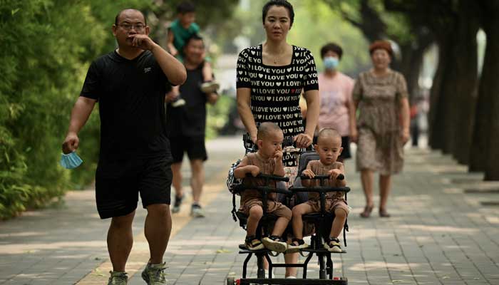 Questa foto scattata il 2 agosto 2022 mostra una donna che spinge un carrello con due gemelli lungo una strada a Pechino.  — AFP