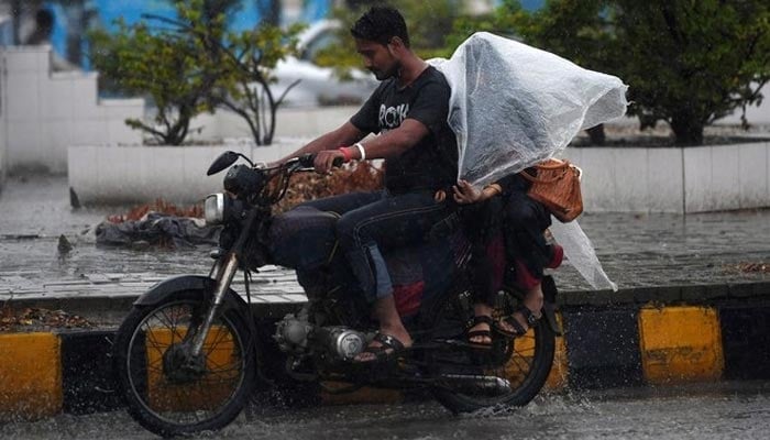 A Pakistani motorcyclist rides on a street as their passenger tries to keep dry under plastic covering during monsoon rain in Karachi on July 29, 2019. — AFP/ File