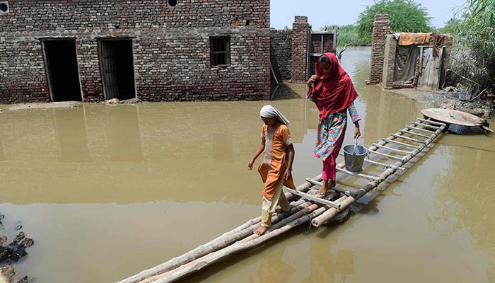 Flood affected people walk on a temporary bamboo path near their flooded house in Shikarpur of Sindh province on August 29, 2022. — AFP