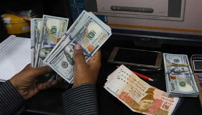 A file image shows a currency dealer counting $100 notes while Rs5,000 notes are placed on the table beside him. — AFP/File