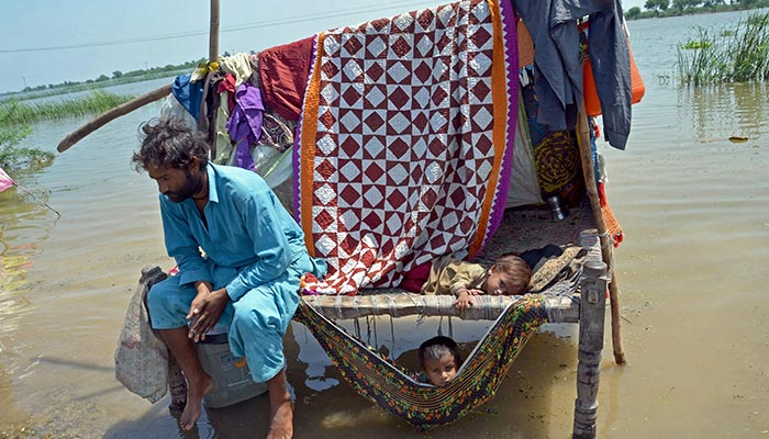Un uomo colpito dall'alluvione siede insieme ai suoi figli accanto alle acque alluvionali dopo le forti piogge monsoniche nel distretto di Jaffarabad, nella provincia del Belucistan, il 31 agosto 2022. — AFP/File