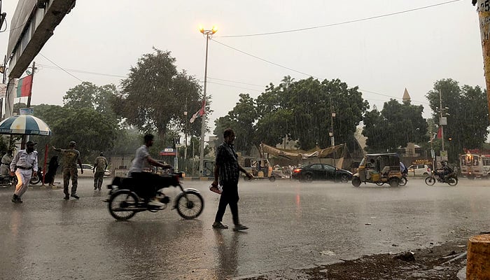 Families on motorcycles drive through a street on a rainy day near Sindh Assembly road in Karachi. —Ashir Ahmed