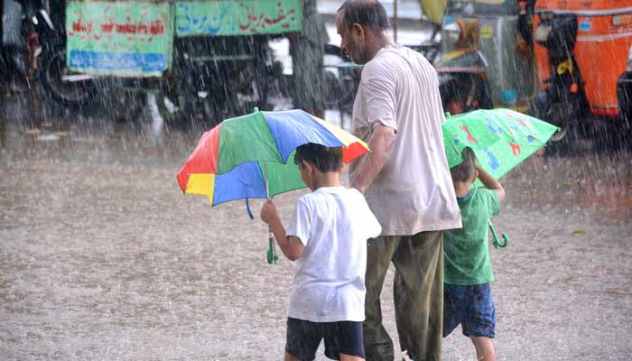 Kids holding umbrellas along with their father are passing through a flooded road amid heavy rain in Karachi on September 13. Photo: APP