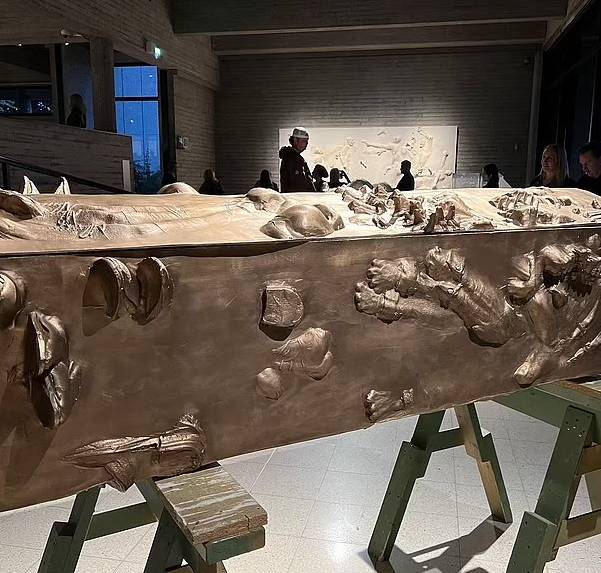 coffin-sized bronze box with hands, feet and faces breaking through structure