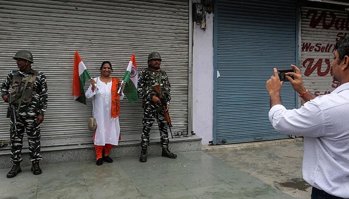 In this photograph taken on August 15, 2022, a man takes a picture of his wife holding Indian national flags next to Indian paramilitary troopers standing guard along a street in Srinagar. — AFP
