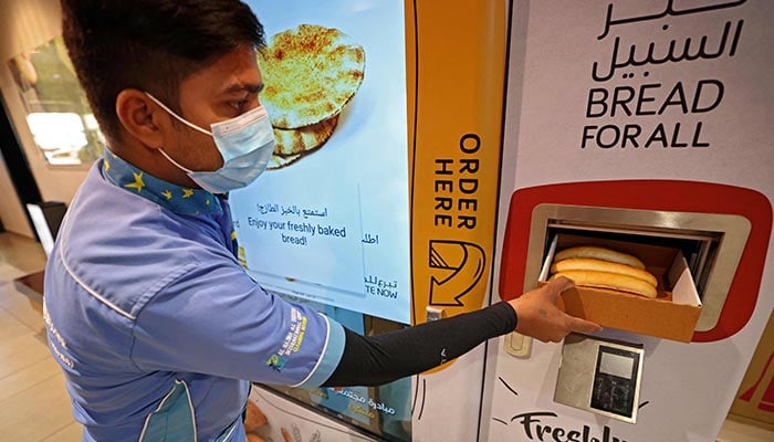 A man collects items from a vending machine that gives out free bread, in Dubai, on September 22, 2022. — AFP